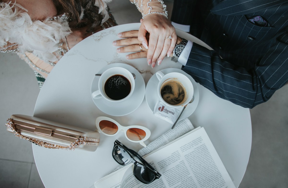 A couple's hands resting on each other over two coffees and a newspaper — intercultural couple dating in Luxembourg