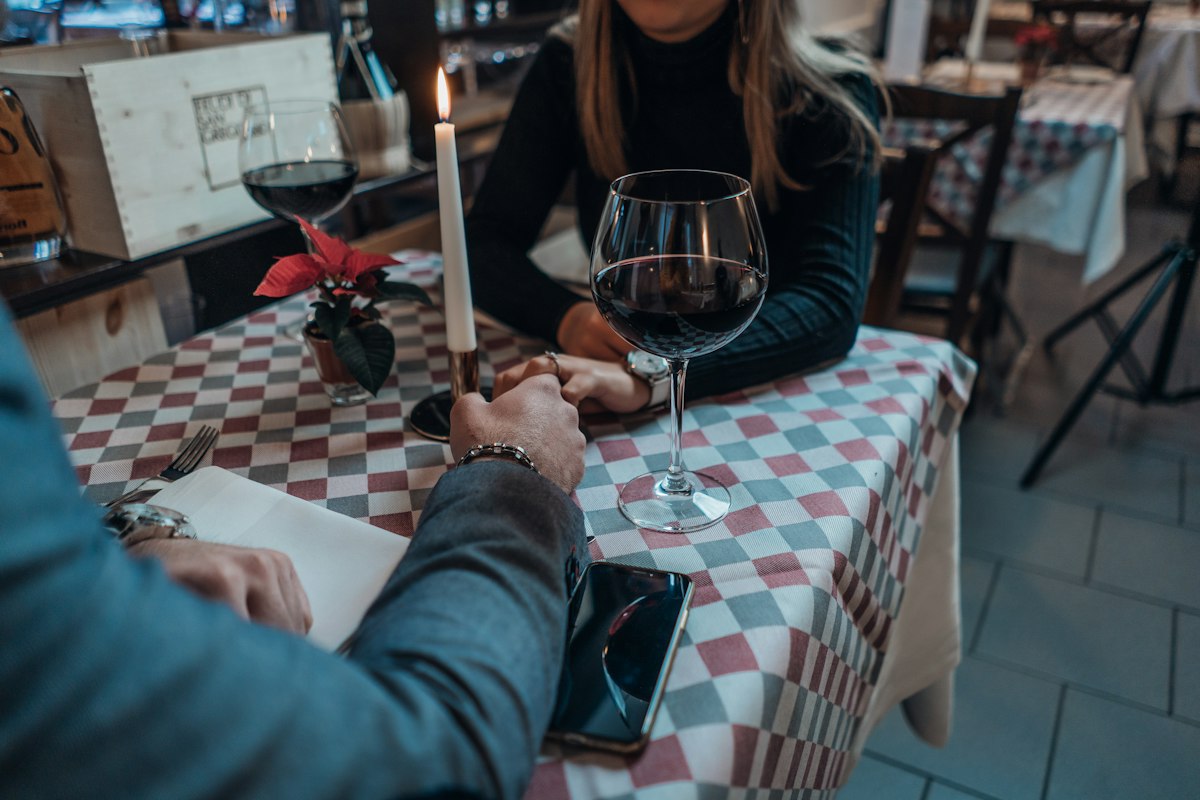 Couple holding hands over dinner with a work phone set aside — serious dating for a finance professional in Luxembourg